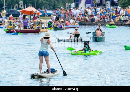 Partyboater mit Frau im Vordergrund auf Paddleboard auf Bayou St. John, New Orleans Stockfoto