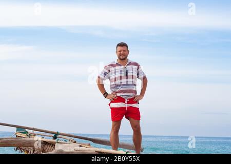 Porträt eines Mannes mit mittlerem Bart im Hemd und roten Shorts auf einem traditionellen Fischerboot Stockfoto