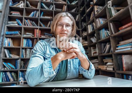 Portrait junger selbstbewusster bärtiger Studentenblogger am Bibliothekstisch Blick auf die Kamera Stockfoto