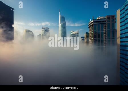 Wolkenkratzer in Jumeirah Lakes Towers (JLT) mit Almas Tower im Nebel bei Sonnenaufgang, New Dubai, Vereinigte Arabische Emirate, Stockfoto