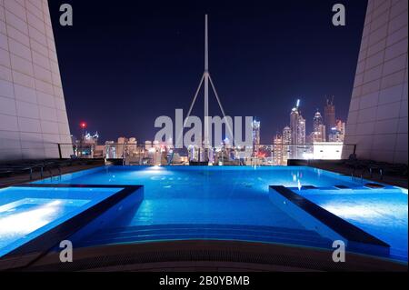 Pool auf dem Dach eines Wolkenkratzers in Jumeirah Lakes Towers (JLT) bei Nacht mit Blick auf die Skyline, New Dubai, Vereinigte Arabische Emirate, Stockfoto