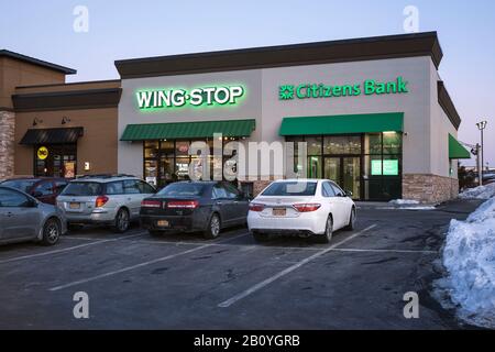 Utica, New York - 21. Februar 2020: Abendansicht von Citizens Bank and Wing Stop Restaurant, Ungezwungene Counterserve-Kette mit verschiedenen Hühnerflügeln Stockfoto