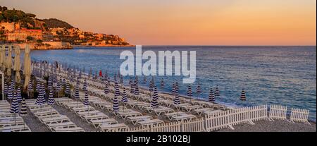 Sonnenuntergang am Strand an der berühmten Promenade des Anglais mit Liegestühlen, Sonnenschirmen und dem Mittelmeer im Hintergrund in Nizza, Südfrankreich Stockfoto