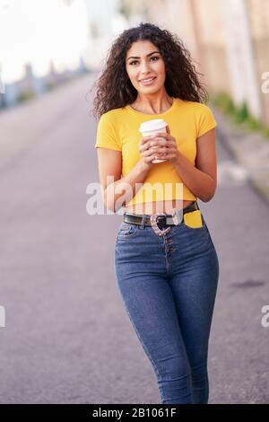 Arabisches Mädchen, das mit einem Kaffee zum Mitnehmen auf der anderen Straßenseite spazieren geht Stockfoto