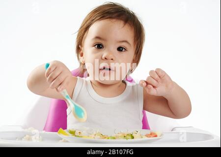 Süßes Baby, das gesunde Lebensmittel auf dem Hochstuhl isst, isoliert Stockfoto