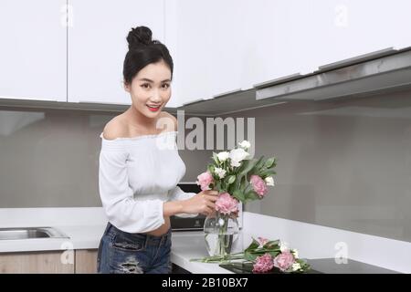 Junge, schöne asiatische Frau, die Blumen in Vase in der Küche arrangierte. Stockfoto