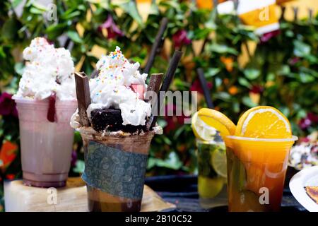 Beim Schwenken wird von Eis und Schokolade mit schütteltem Schütteln zu gesundem Orangensaft mit Scheiben im Glas mit grünem Blattgrund geschossen Stockfoto