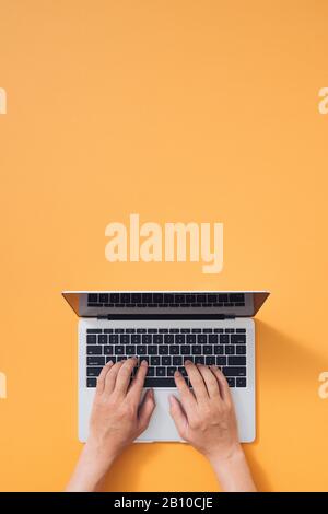 Flaches Lay aus Laptop, Kaffee und Notebook auf gelbem Hintergrund. Tastatur mit männlichen Händen Stockfoto