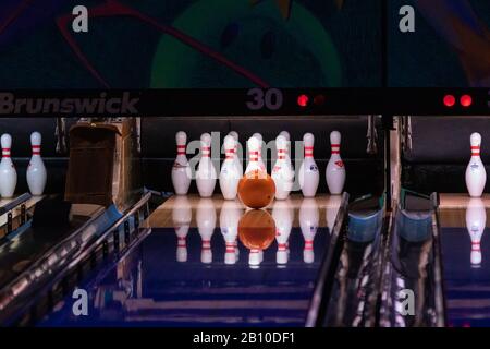 Hillsboro, Oregon USA - 16. März 2019: Der orangefarbene Bowlingball soll am Ende einer Bowlingbahn, die auf einer polierten Fahrbahn reflektiert, in die Mitte der Pins schlagen Stockfoto