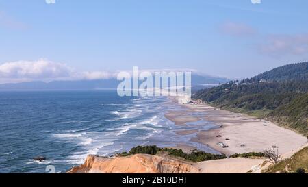 Malerische Aussicht auf Cape Kiwanda State Natural Area. Autos auf einem Sandstrand geparkt, Menschen genießen sonniges Wetter. Wellen krachen an einem Strand Stockfoto