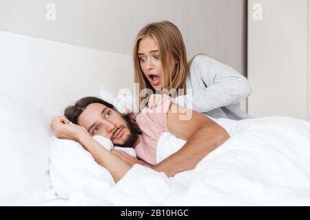 Schönes junges Paar, das zuhause im Bett liegt, schockierte Mädchen, die ihren Freund morgens aufwachen Stockfoto