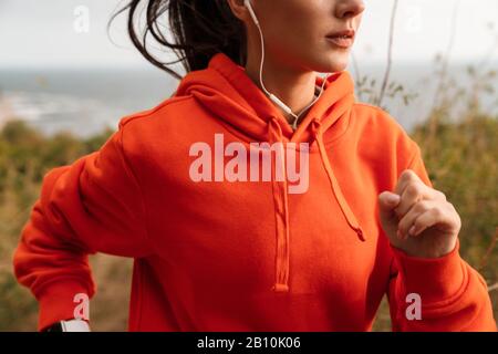 Zugeschnittenes Bild einer attraktiven jungen brünette Sportlerin mit Hoodie Joggen im Freien an einer Küste Stockfoto