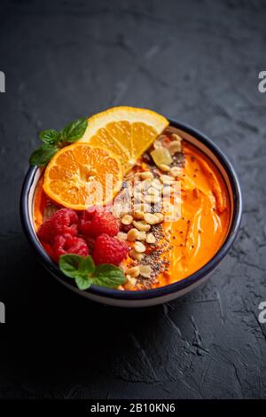 Schüssel mit frischem, gesundem Smoothie oder Joghurt. Mit orangefarbenen Scheiben, Mandarine, Himbeere, chia und Nüssen Stockfoto