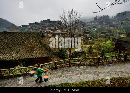 Miao Woman trägt Lebensmittelabfälle in Xijiang, dem traditionellen Dorf der ethnischen Minderheit der Miao. Provinz Guizhou, China Stockfoto