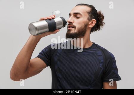 Bild des jungen bärtigen Mannes in Sportbekleidung Trinkwasser isoliert über weißem Hintergrund Stockfoto