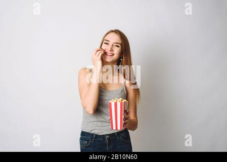 Mädchen im Studio mit Popcorn herumtören. Porträt eines lachenden Mädchens, das Popcorn hält und die Kamera über weißem Hintergrund isoliert betrachtet. Stockfoto