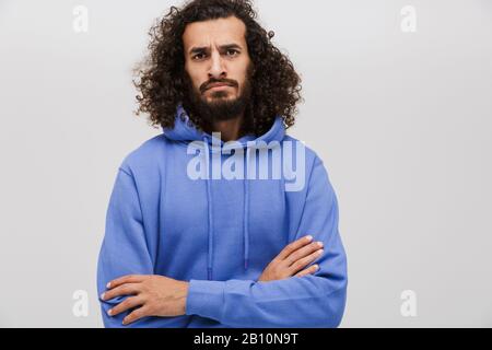 Bild des wütenden unshaven Mannes in legeren Sweatshirt, das mit über weißem Hintergrund isolierten Armen steht Stockfoto