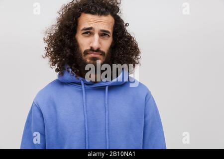 Bild eines frustrierten, unrasierten Mannes in einem lässigen Sweatshirt, das an der Kamera auffrötet, isoliert über weißem Hintergrund Stockfoto