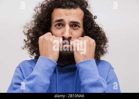 Bild eines eingeschüchterten, unrasierten Mannes in einem lässigen Sweatshirt, das Angst vor der Kamera ausdrückt, isoliert über weißem Hintergrund Stockfoto