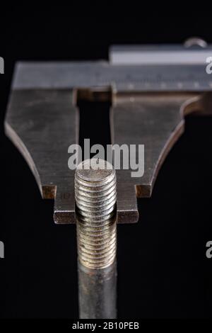 Messung des Bremssattels mit Schraubendurchmesser. Messzubehör in der Zimmerei. Dunkler Hintergrund. Stockfoto