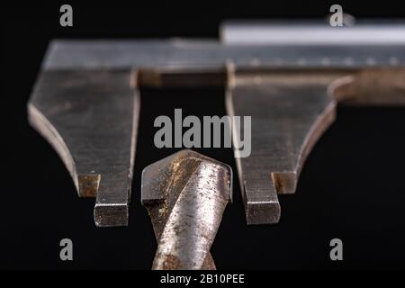 Messung des Bremssattels mit Bohrerdurchmesser. Messzubehör in der Zimmerei. Dunkler Hintergrund. Stockfoto