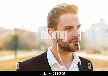 Nahaufnahme eines attraktiven jungen Geschäftsmannes, der Ohrhörer über den Hintergrund der Stadt trägt Stockfoto