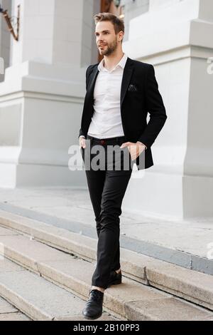 Gutaussehender junger, lächelnder Geschäftsmann, der auf der Straße in der Stadt spazieren geht und Anzug trägt Stockfoto