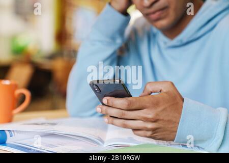 Nahaufnahme eines ernsthaften afrikanischen Jungen, der im Innenbereich mit dem Handy an der Drehscheibe sitzt Stockfoto