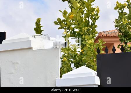 Überwachungskamera an der weißen Außenwand eines Hauses und neben einem Zaun mit Stacheln Stockfoto