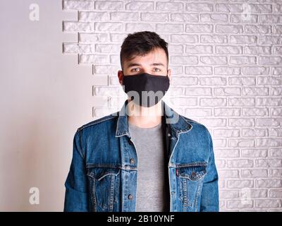 Junger Mann in medizinischer Maske gegen weiße Wand Stockfoto