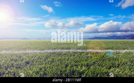 Rasenplatz, frisches grünes Rasensportgelände, blau bewölkter Himmel. Nahansicht von Gras, verwackelte Hintergrundfarbe im Querformat