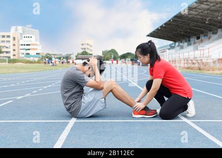 junges asiatisches Paar macht Sit-ups auf der blauen Laufstrecke im Stadion Stockfoto