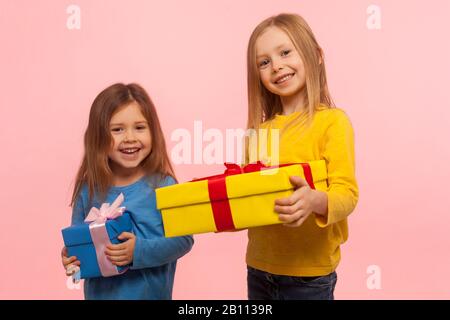 Geschenk für jedes Kind. Zwei fröhliche, charmante kleine Mädchen, die umhüllte Kisten halten und lächeln, vor der Kamera lachen, Geburtstagsgeschenke genießen, weihnachtsurlauber Stockfoto