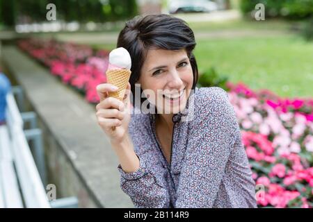 Lachende Frau sitzt auf der Bank und isst Eis Stockfoto