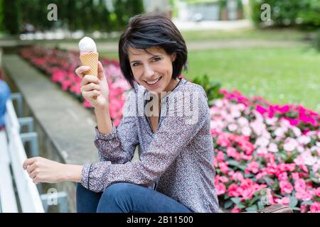 Lachende Frau sitzt auf der Bank und isst Eis Stockfoto