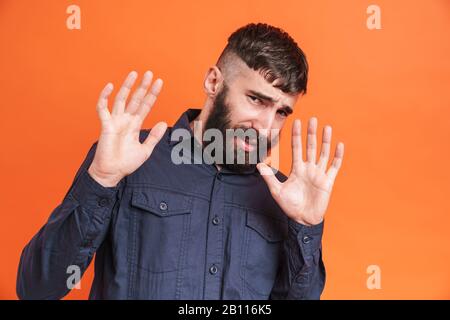 Bild Nahaufnahme des nervösen Mannes mit Nasenschmuck, das schwarze Hemd trägt, hebt Arme und macht Stopp-Gesten isoliert über orangefarbenem Hintergrund Stockfoto