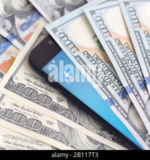 Charkow, UKRAINE - 6. FEBRUAR 2020: Smartphone-Bildschirm mit Facebook-App und vielen Hundert Dollar-Rechnungen. Business- und Social Networking-Konzept Stockfoto