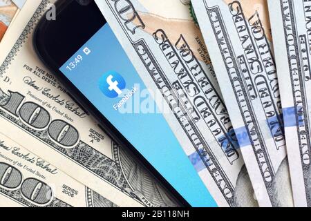 Charkow, UKRAINE - 6. FEBRUAR 2020: Smartphone-Bildschirm mit Facebook-App und vielen Hundert Dollar-Rechnungen. Business- und Social Networking-Konzept Stockfoto