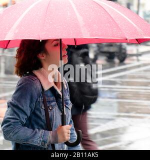 Belgrad, Serbien - 24. September 2019: Eine junge Frau in Denimjacke, die an einem regnerischen Tag unter rotem Schirm spaziert Stockfoto