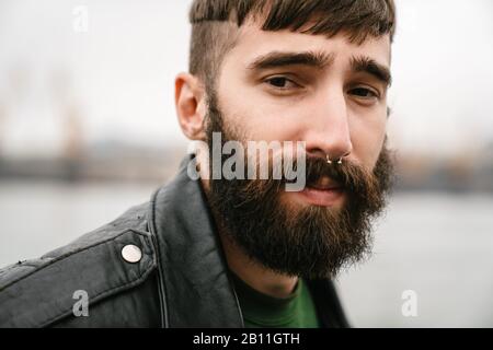 Fotoaufnahmen von bärtigen jungen Männern, die Lederjacke tragen und die Kamera im Freien betrachten Stockfoto