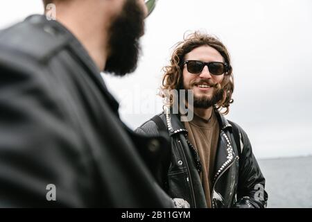 Foto von bärtigen fröhlichen Männern Biker in Sonnenbrille lächeln und reden, während sie im Hafen stehen Stockfoto