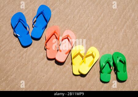Eine Gruppe von Flip-Flops in hellen Sommerfarben, die am glatten Sandstrand sitzen Stockfoto