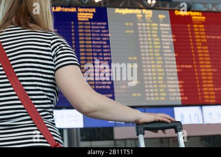 Frau schaut auf die Anzeigetafel am Flughafen. Wählen Sie ein Land für Reisen oder Migration aus. Stockfoto