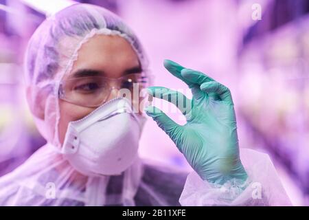 Arzt in Schutzkleidung und in Schutzhandschuhen, der das Medikament in der Hand untersucht Stockfoto