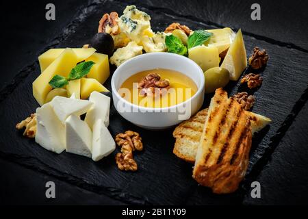 Käseplatte mit Käsesorten Dorblu, Parmesan, Brie, Camembert und Roquefort auf schwarzem, strukturiertem Hintergrund Stockfoto