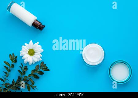 Set mit Kosmetikflaschen auf blauem Hintergrund. Cremefarbene und weiße Lotion mit Gänseblümchen. Natürliche Pflanzenkosmetik. Glasbecher und Spray mit weißem c Stockfoto