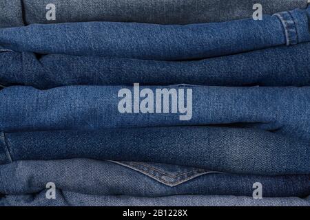 Jeans-Stapel in Denimblau, in klassischem Indigo-Stil in verschiedenen Farben. Nahaufnahme, Modekonzept, Hintergrund. Stockfoto