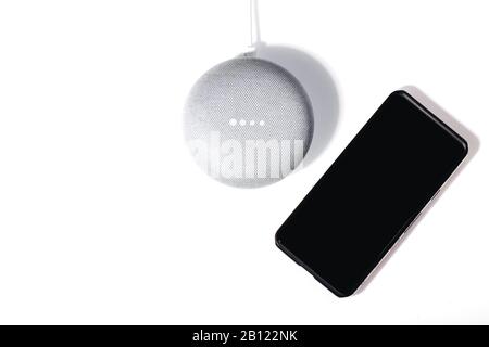Digital Assistant-Konzept. Flacher Lautsprecher mit aktivierten LED-Leuchten und isoliertem Smartphone auf weißem Hintergrund. Stockfoto