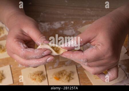 Eine Frau sculpt Knödel und Ravioli aus Kneten und Kohl. Sperrholzschneidplatte, Holzmehlsieb und Walzstift aus Holz - Werkzeuge für Stockfoto