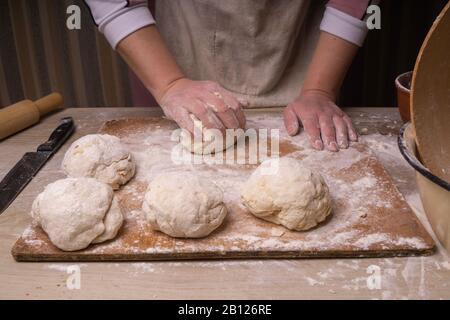 Eine Frau knetet den Teig. Sperrholzschneidebrett, Holzmehlsieb und Walzstift - Werkzeuge zur Herstellung von Teig. Stockfoto